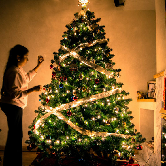 child-standing-in-front-of-Christmas-tree-with-string-lights